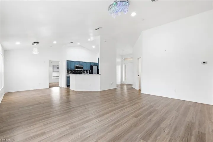 Unfurnished living room featuring hanging lights, lofted ceiling, and light wood finished floors