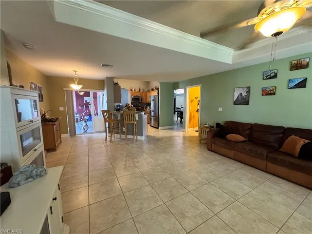 Living area with a ceiling fan, a tray ceiling, light tile patterned flooring, and crown molding