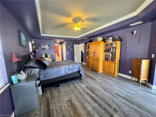 Bedroom featuring a tray ceiling, crown molding, wood finished floors, and ceiling fan