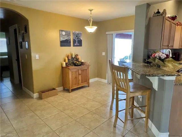 Kitchen featuring arched walkways, a breakfast bar, decorative light fixtures, a peninsula, and dark stone counters