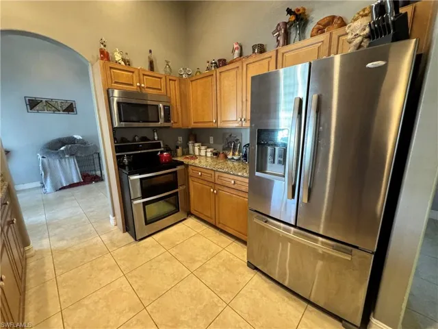 Kitchen featuring stainless steel appliances, light stone countertops, light tile patterned flooring, wood finish cabinetry, and arched walkways