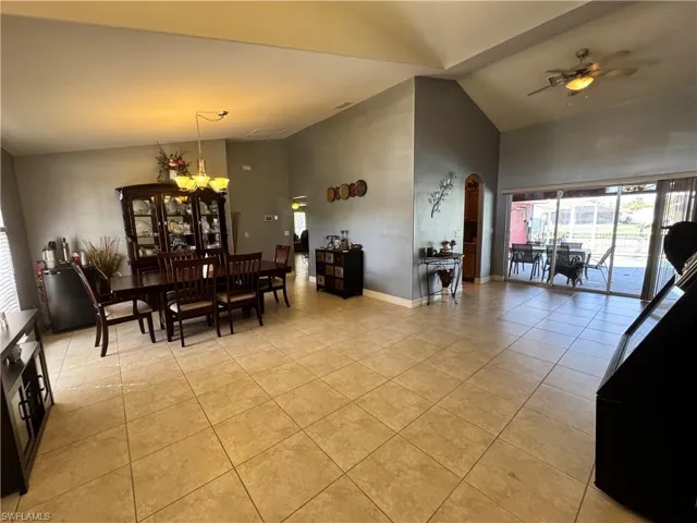 Dining space featuring vaulted ceiling, plenty of natural light, a ceiling fan, light tile patterned floors, and arched walkways