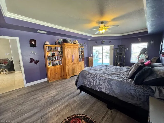 Bedroom featuring a raised ceiling, access to exterior, dark wood-type flooring, ceiling fan, and ornamental molding