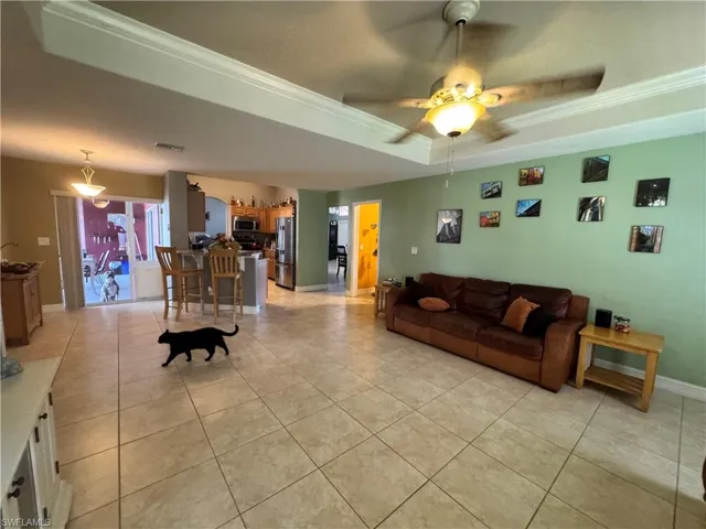 Living room featuring a tray ceiling, ceiling fan, crown molding, and light tile patterned flooring