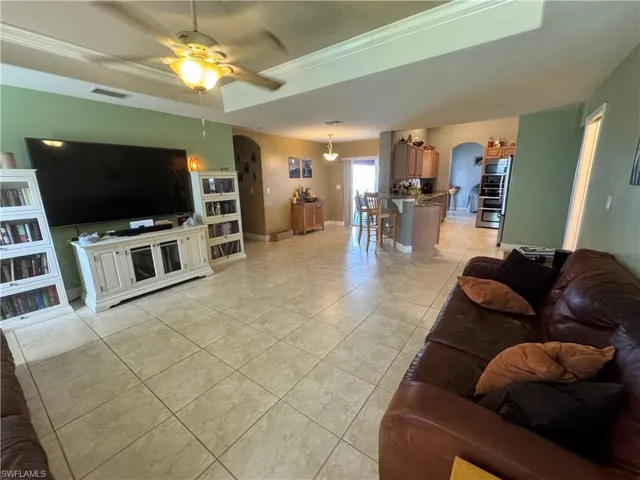 Living area with a tray ceiling, crown molding, arched walkways, light tile patterned flooring, and a ceiling fan