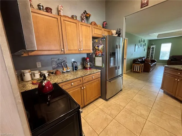 Kitchen with black range with electric stovetop, light stone counters, open floor plan, wood finish cabinetry, and stainless steel refrigerator with ice dispenser