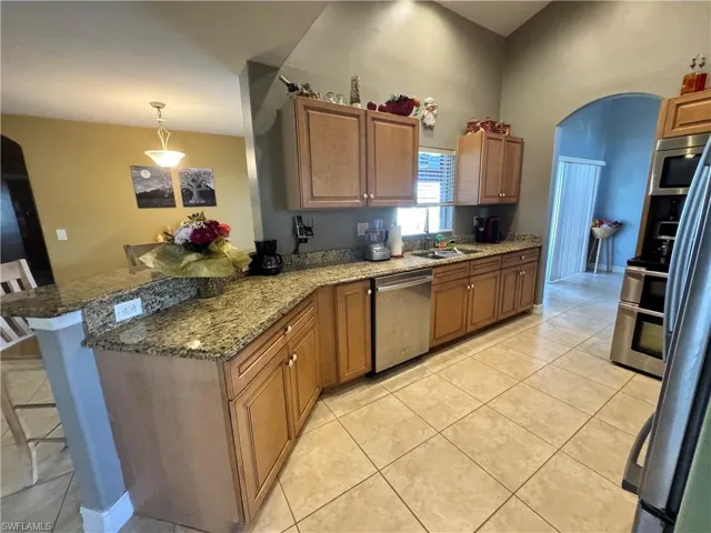 Kitchen featuring arched walkways, wood finish cabinets, a peninsula, dark stone counters, and stainless steel appliances