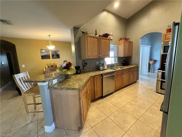 Kitchen featuring arched walkways, wood finish cabinetry, a kitchen bar, stainless steel appliances, and a high ceiling
