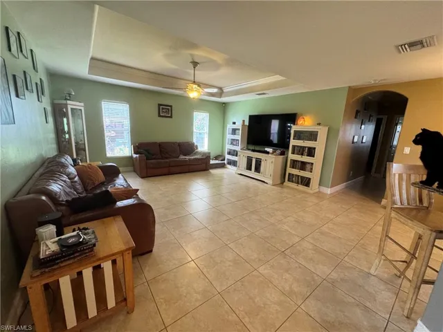 Living room with arched walkways, a raised ceiling, a ceiling fan, and light tile patterned floors