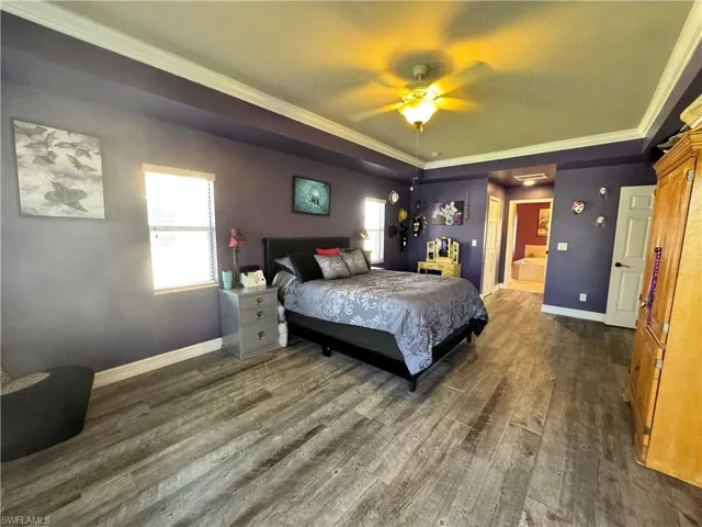 Bedroom with crown molding, multiple windows, dark wood-type flooring, connected bathroom, and a ceiling fan