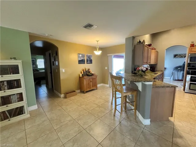 Kitchen featuring arched walkways, dark stone countertops, a kitchen bar, light tile patterned floors, and hanging light fixtures
