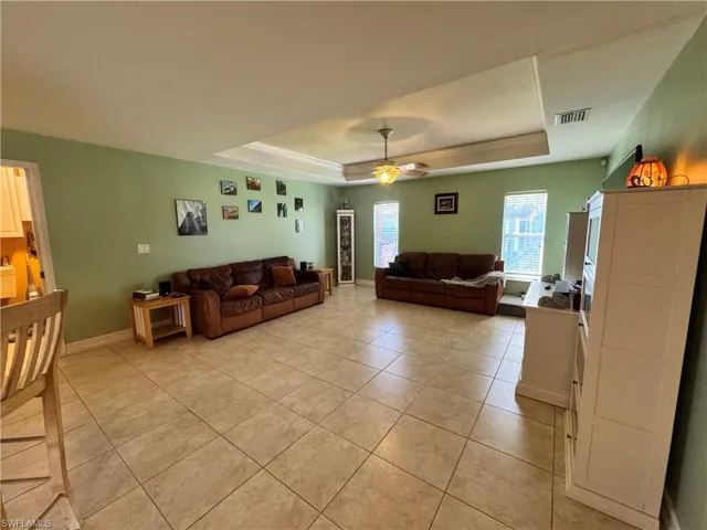 Living area with a tray ceiling, a ceiling fan, and light tile patterned floors