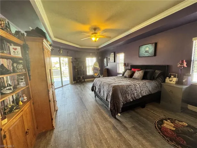 Bedroom with a tray ceiling, dark wood-type flooring, ornamental molding, access to outside, and ceiling fan