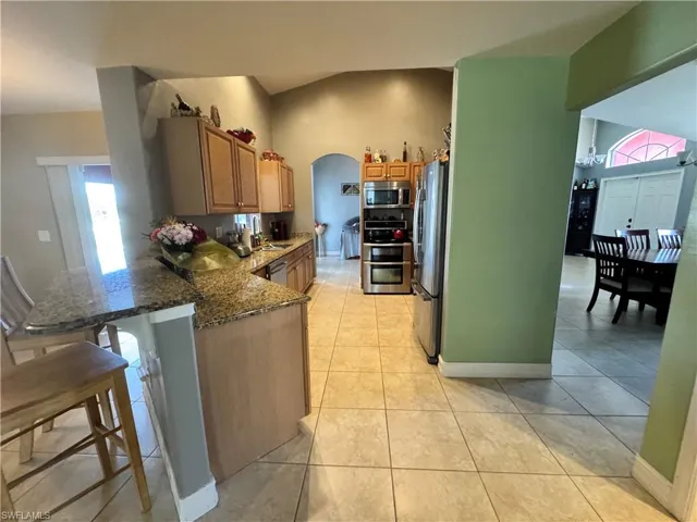 Kitchen featuring dark stone counters, a peninsula, stainless steel appliances, arched walkways, and a kitchen bar