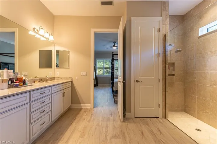 Bathroom with tiled shower, wood-type flooring, vanity, and plenty of natural light