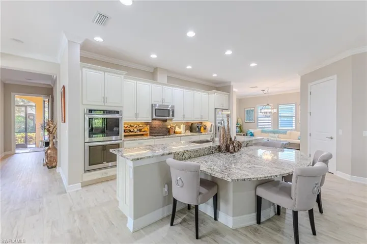 Kitchen with appliances with stainless steel finishes, a kitchen breakfast bar, pendant lighting, a large island, and white cabinets