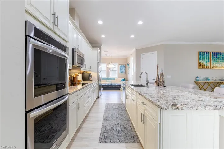 Kitchen featuring sink, crown molding, a large island with sink, appliances with stainless steel finishes, and light stone countertops
