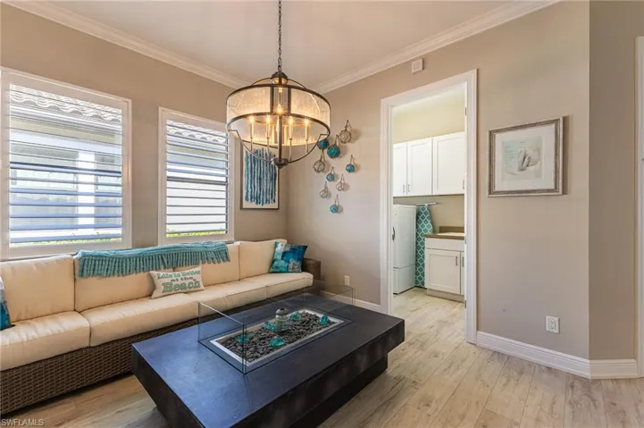Living room with ornamental molding, washer / dryer, light hardwood / wood-style flooring, and a notable chandelier