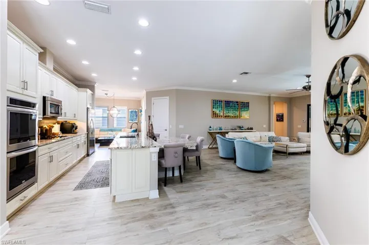 Kitchen featuring a breakfast bar, a kitchen island with sink, white cabinetry, stainless steel appliances, and light stone counters