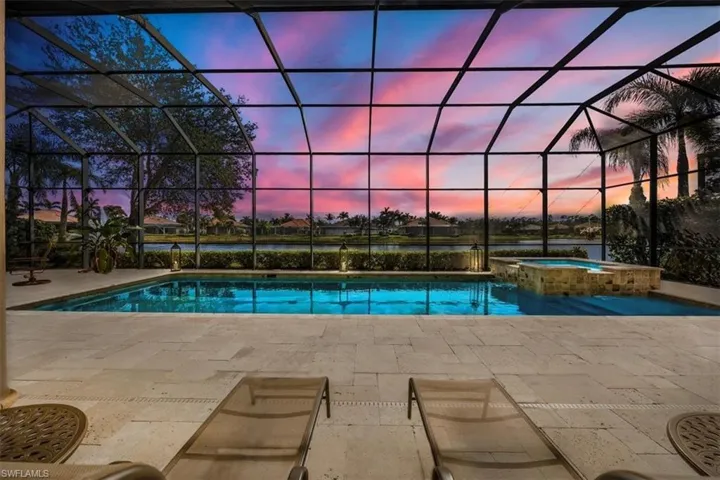 Pool at dusk featuring a lanai, a water view, a patio area, and a pool with connected hot tub
