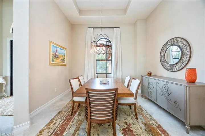 Dining room featuring baseboards, a chandelier, and a raised ceiling