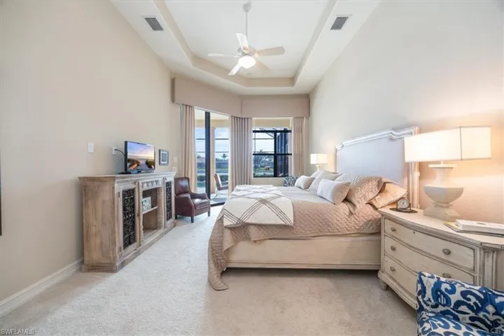 Bedroom with a tray ceiling, visible vents, a ceiling fan, and light carpet