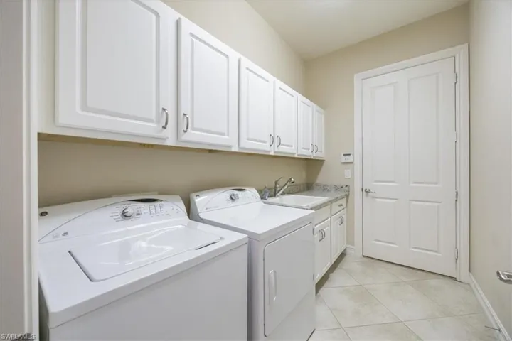 Clothes washing area with a sink, light tile patterned flooring, independent washer and dryer, baseboards, and cabinet space