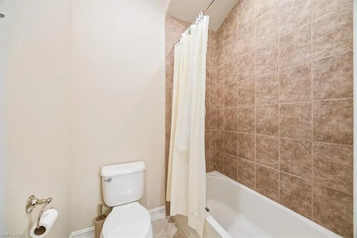 Bathroom featuring shower / tub combo with curtain, toilet, and baseboards