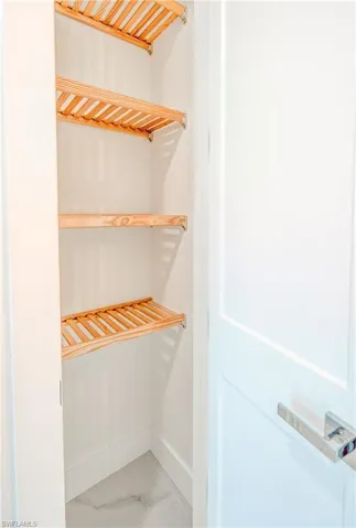 Built-in slatted wood shelving, marble-look tile flooring, white interior walls, and a contemporary door with a lever handle