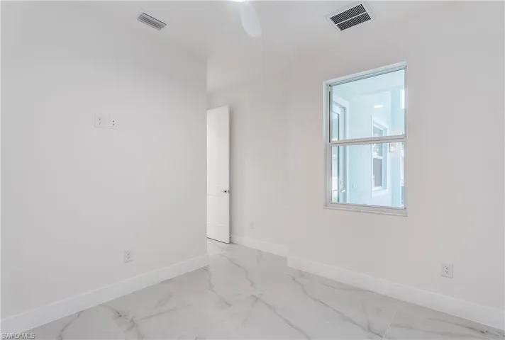 White interior walls, large window, white ceiling fan, white baseboards, and white-finish flooring