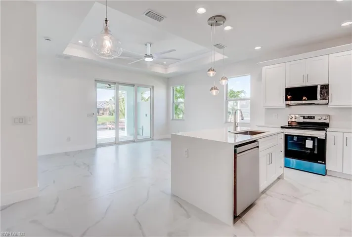 Open-concept living space with large format tile flooring, a kitchen island with integrated sink, stainless steel appliances, and a tray ceiling with recessed lighting