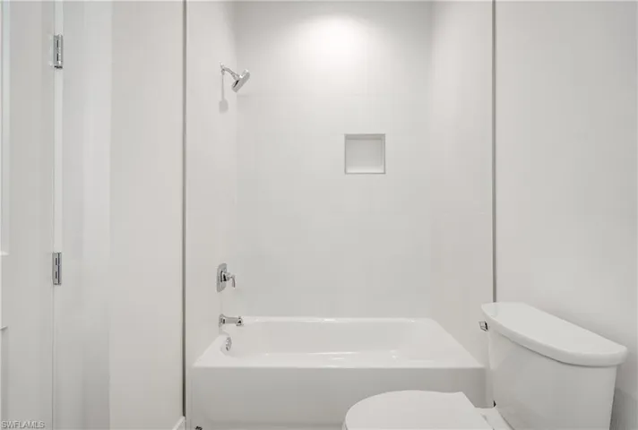 Bathtub with polished chrome fixtures and integrated wall niche, complemented by full-height white tile surround