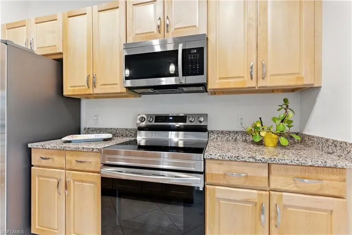 Kitchen featuring stainless steel appliances, light brown cabinetry, light stone countertops, and tile patterned floors