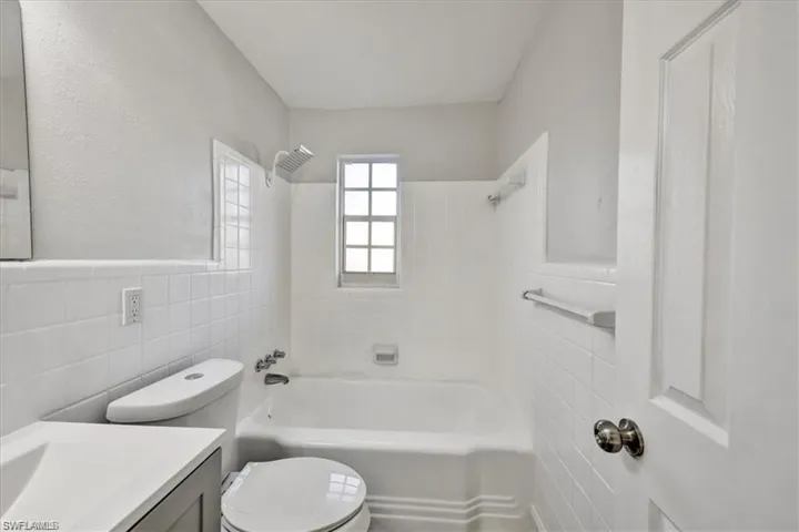 Full bathroom with tile walls, vanity, toilet, shower / washtub combination, and a wainscoted wall