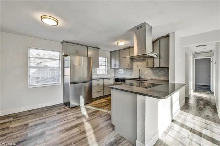Kitchen featuring stainless steel appliances, wall chimney exhaust hood, gray cabinets, a sink, and a peninsula