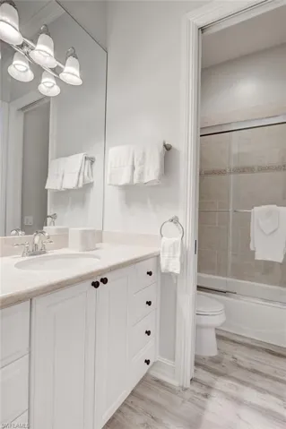 Full bathroom featuring hardwood / wood-style flooring, vanity, toilet, and bath / shower combo with glass door
