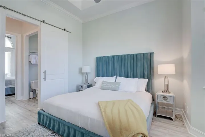 Bedroom featuring light wood-type flooring, a barn door, and crown molding