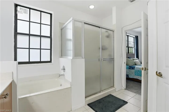 Bathroom featuring a built-in tub, a frosted glass shower enclosure with sliding doors, a black grid window, and recessed lighting