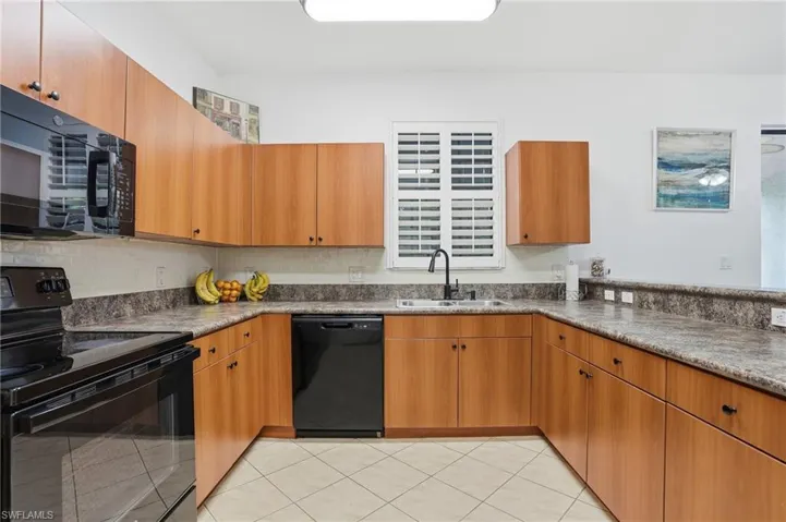 U-shaped kitchen featuring wood-finish cabinetry, black appliances, a double basin sink with a gooseneck faucet, and solid surface countertops