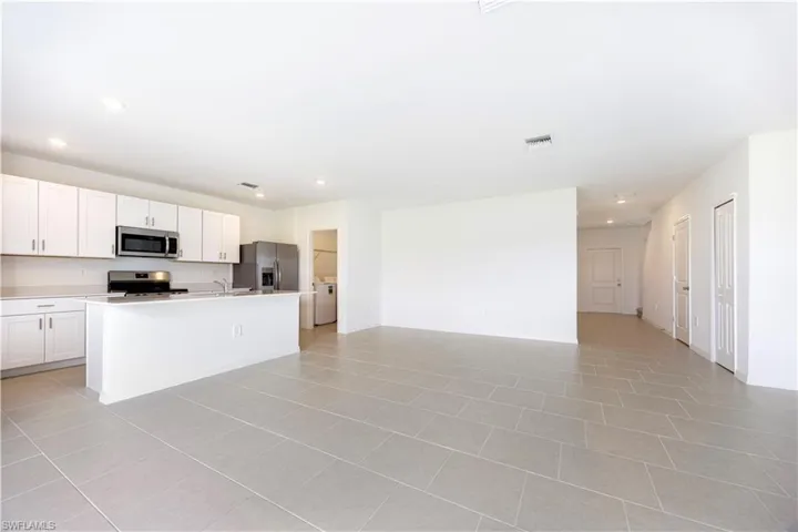 Kitchen with white cabinetry, open floor plan, light countertops, stainless steel appliances, and a kitchen island with sink