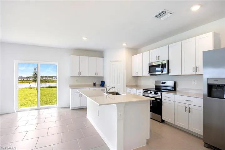 Kitchen featuring stainless steel appliances, white cabinetry, an island with sink, light tile patterned flooring, and recessed lighting