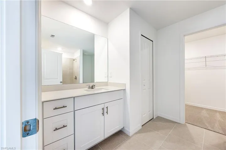 Bathroom featuring vanity, a spacious closet, light tile patterned floors, a tile shower, and recessed lighting