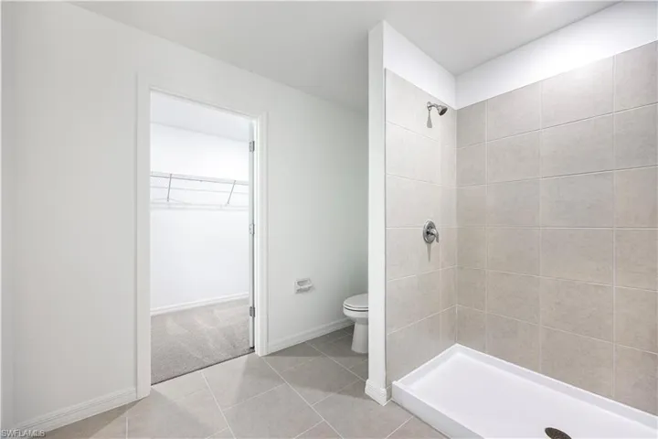 Bathroom featuring a walk in closet, light tile patterned flooring, and a shower stall
