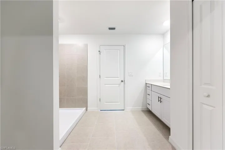 Bathroom featuring vanity, tiled shower, light tile patterned flooring, and a closet