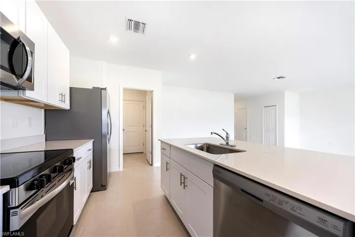 Kitchen featuring stainless steel appliances, white cabinetry, light stone counters, recessed lighting, and light tile patterned floors