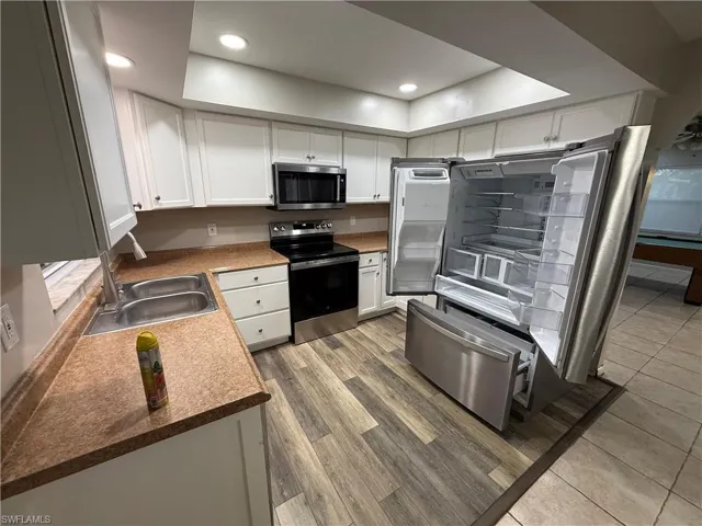 Kitchen with white cabinetry, stainless steel appliances, recessed lighting, light wood finished floors, and dark countertops