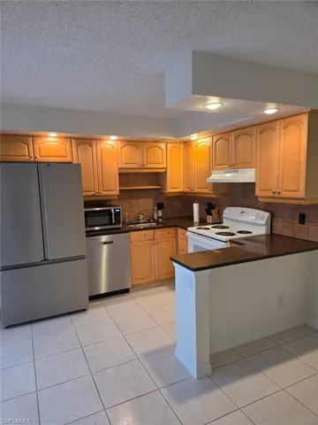 Kitchen with appliances with stainless steel finishes, a textured ceiling, under cabinet range hood, a peninsula, and light tile patterned floors