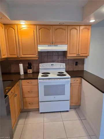 Kitchen featuring electric stove, under cabinet range hood, light tile patterned floors, recessed lighting, and backsplash