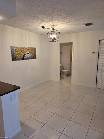 Unfurnished dining area with a textured ceiling, a chandelier, and light tile patterned flooring
