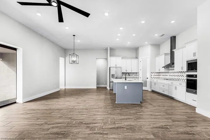 Kitchen with white cabinetry, gray cabinets, tasteful backsplash, stainless steel appliances, and a center island with sink